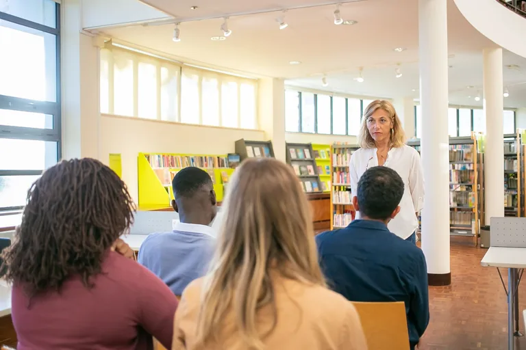 A tutor speaking with a small group of adult learners in a library classroom
